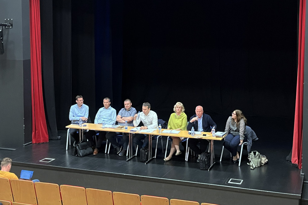 Predstavniki ministrstva in občine sedijo za mizami v konferenčni dvorani ali podobnem okolju, pred njimi pa so v vrstah posedeni občani in druga zainteresirana javnost.