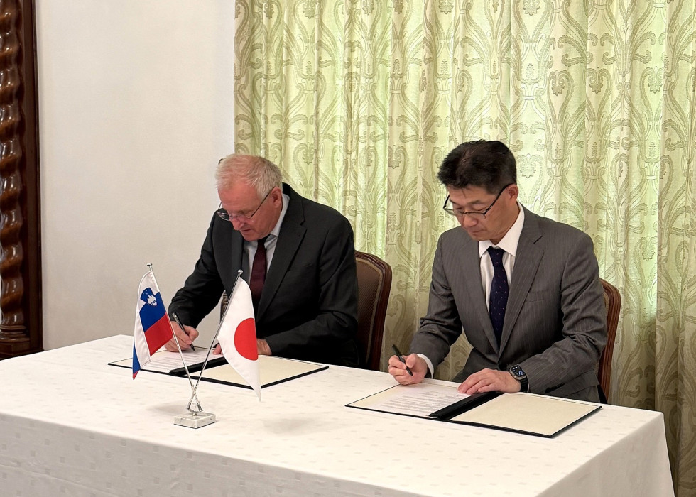 Dva moška sedita za mizo in podpisujeta dokumente