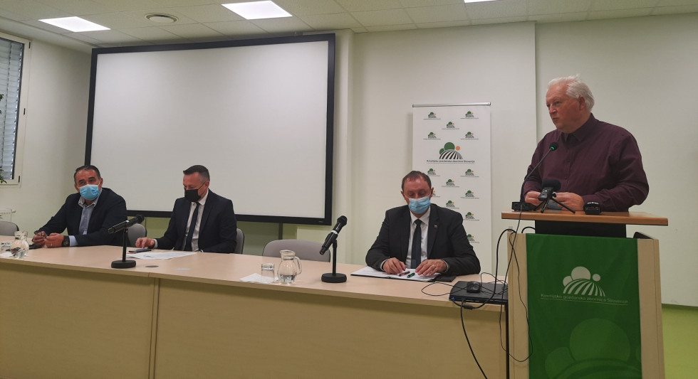 Vidna sta dva predstavnika Kmetijsko gozdarske zbornice Slovenije in dva predstavnika Agencije Republike Slovenije za kmetijske trge in razvoj podeželja, kateri sedijo za mizo in govorniškim pultom ter se pripravljajo za izvedbo novinarske konference.