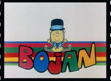 Bojan the Bear is standing in front of the rainbow, his name is written in capital letters in front of him.