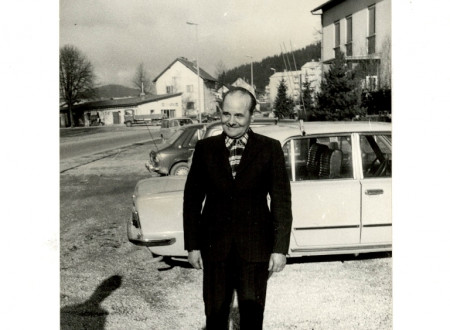 Črno-bela fotografija Janeza Rusa v slavnostni obleki pred belim avtomobilom. V ozadju so vidne hiše in travnik.