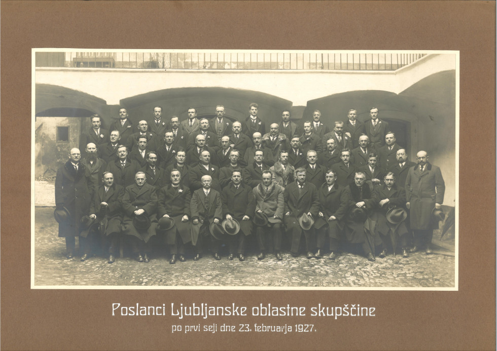 Assembly members pose for a photographer, wearing coats and holding hats in their hands.