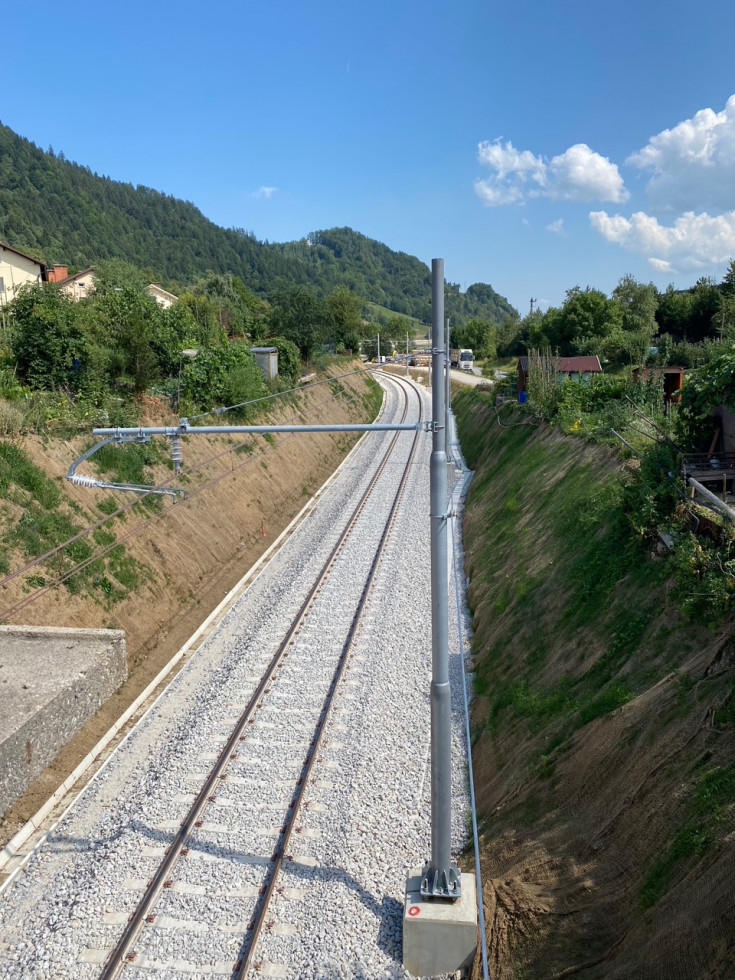 Nadgrajen odsek Lesce Bled-Jesenice, na desni drog, na levi strehe hiš, v ozadju vzpetina