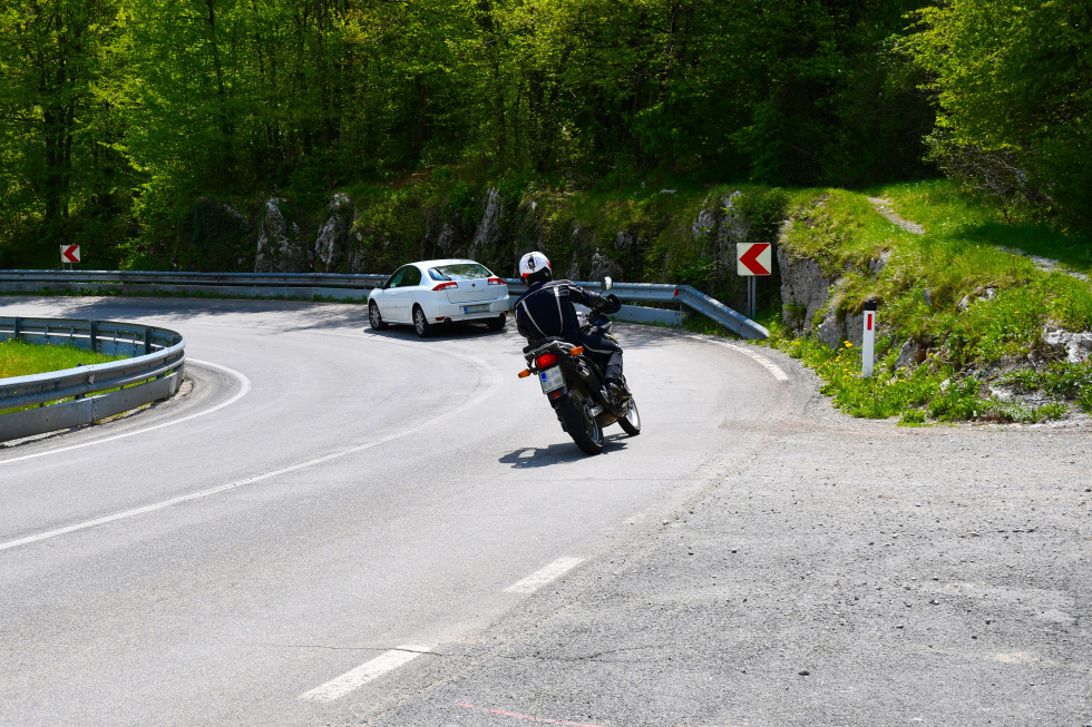 Motorist in avtomobil v ostrem zavoju v levo. Z desne strani stranska cesta. Pesek na vozišču.