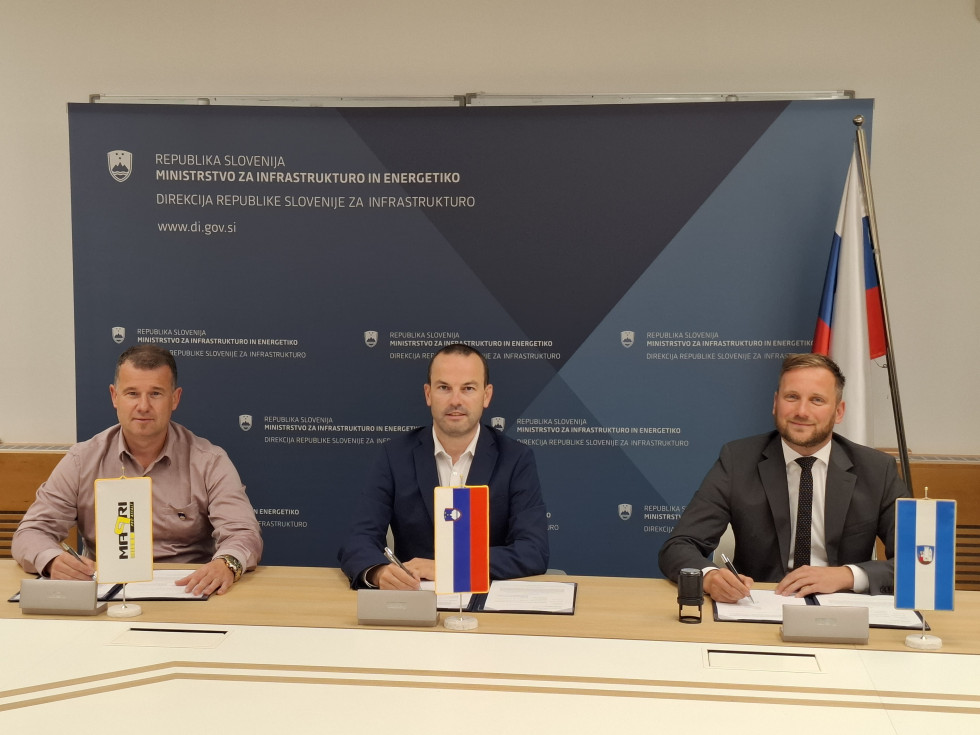 Trije moški sedijo za mizo, s pisali v roki, tik pred podpisom pogodbe.