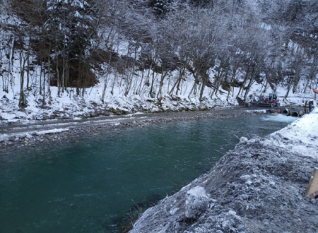 Reka Sora teče, na brežini pa je viden delovni stroj 