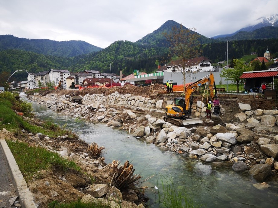 Slika struge in bagra, ki izvaja dela, v ozadju so bloki