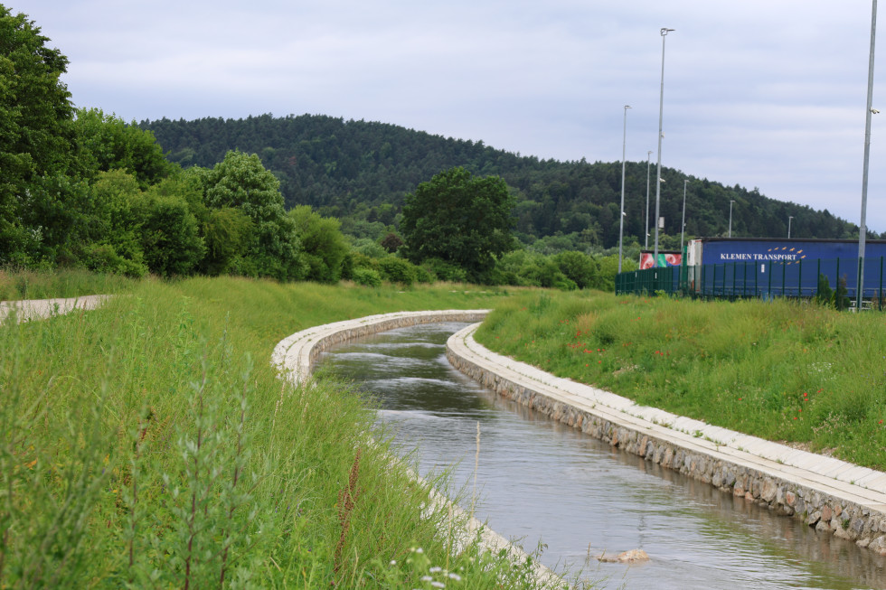 Urejena vodna struga poteka skozi zeleno krajino ob travnatih brežinah.