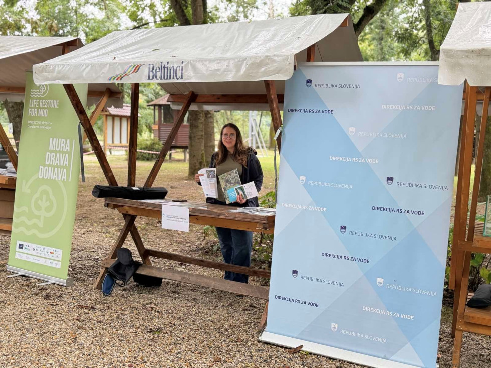 Poteka predstavitev projekta LIFE RESTORE for MDD obiskovalcem na stojnici DRSV v Ižakovcih. Ženska stoji pri stojnici.