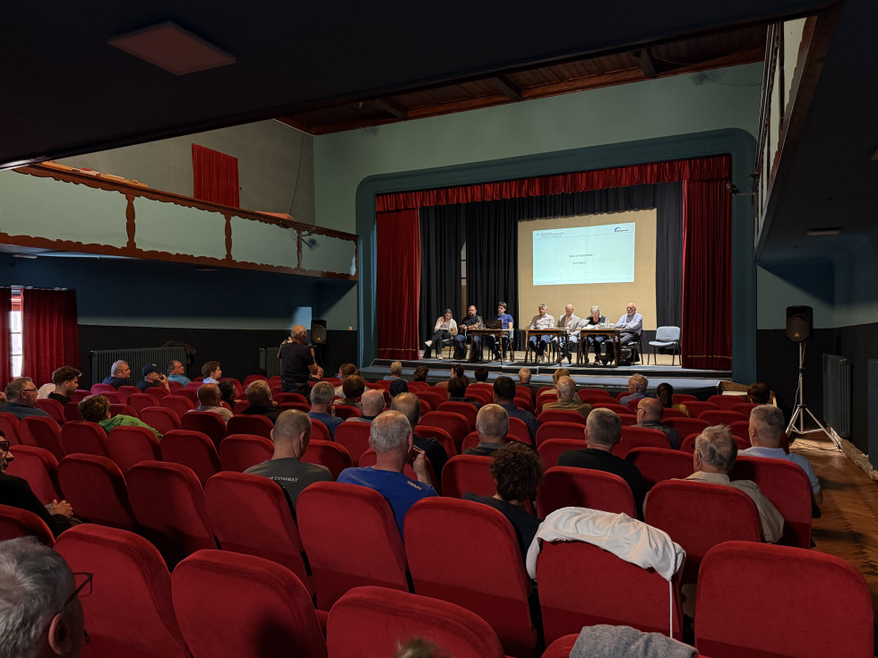 Udeleženci sedijo v dvorani in spremljajo dogodek ob projekciji predstavitve na odru.