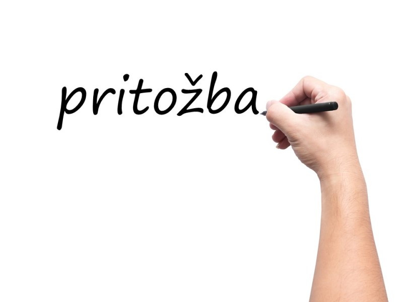 Slika je simbolična. Prikazuje roko s pisalom, ki je napisala besedo "pritožba".