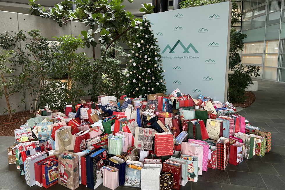 Tabla Finančne uprave, zraven božično drevo, pod njim pa velik kup daril