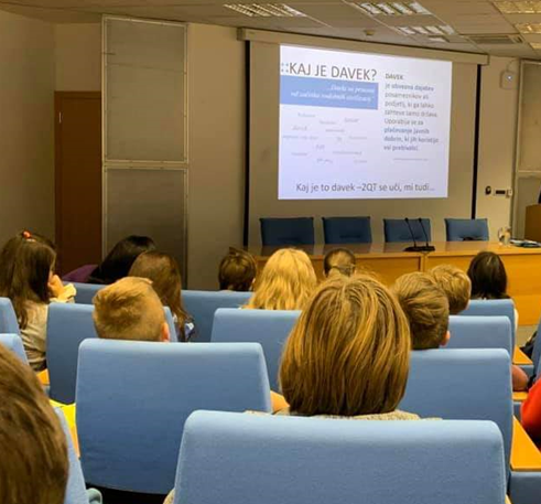 Otroci, ki poslušajo predavanje in gledajo prezetacijo o davkih. 