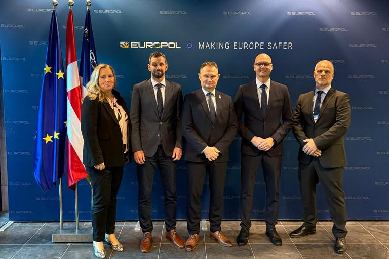 Dva predstavnika Finančne uprave in trije predstavniki Policije Stojijo pred zastavami EU, Danske in EUROPOL-a 