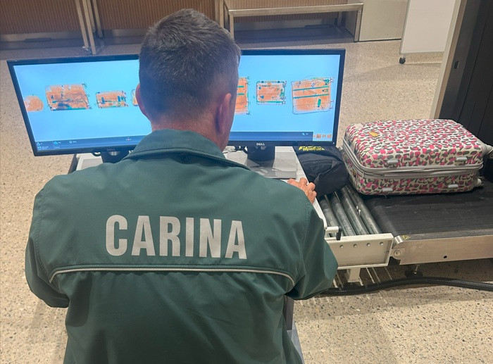 carinik prek posebne naprave za skeniranje pregleduje vsebino potovalnega kovčka