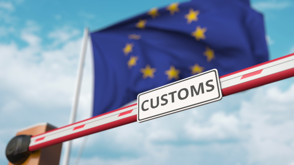 Simbolična slika zapornice, na kateri je napis Customs, zadaj pa je zastava EU