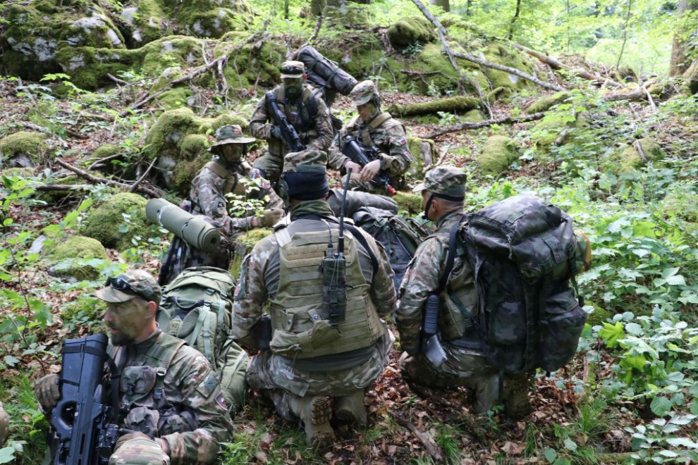 Vojaki v gozdu sedijo v krogu in se pripravljajo na nalogo