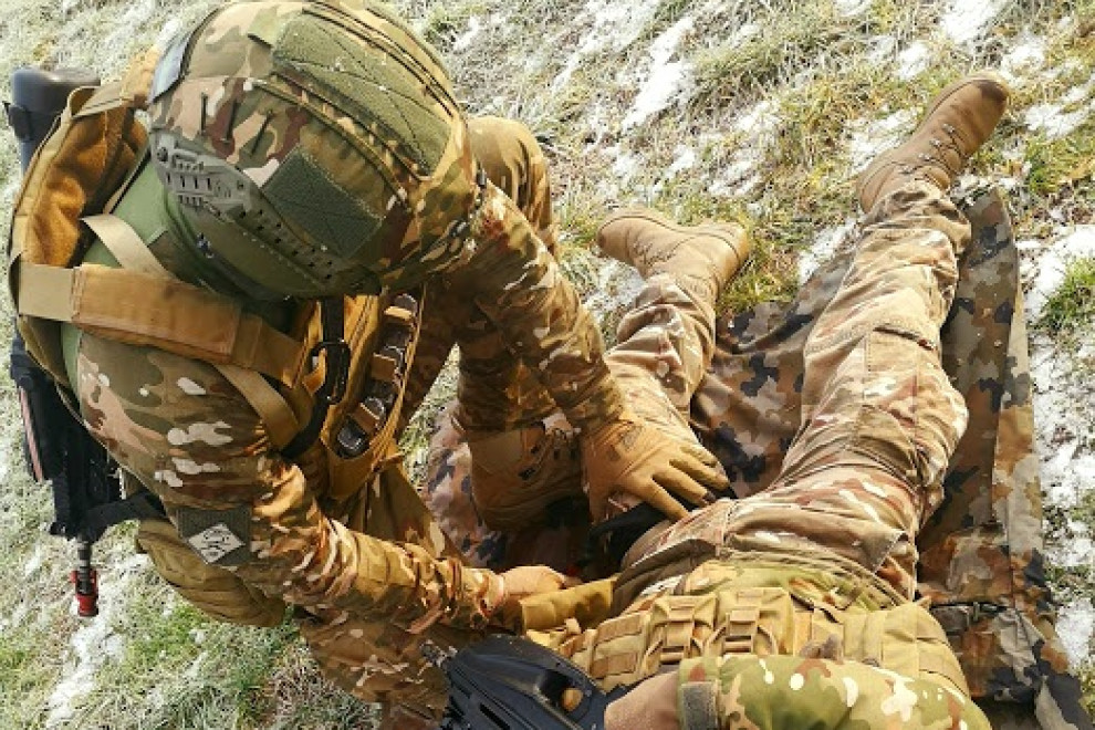 Vojak preverja pri poškodovanem vojaku poškodbo in nudi prvo pomoč.