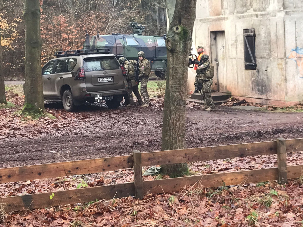 Pripadniki Slovenske vojske pred stavbo ob prisotnosti ocenjevalca  izvajajo postopke vstopa v vojaško vozilo Toyota.