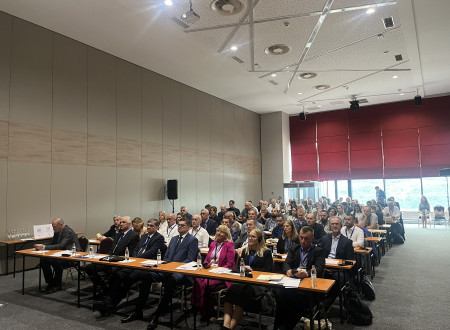 Udeleženci konference sedijo v konferenčni dvorani za mizami v desetih vrstah
