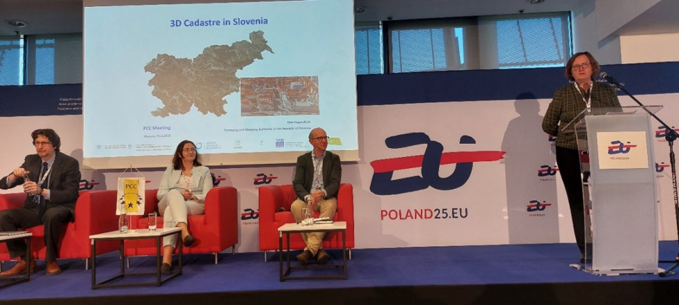 Oder, na katerem ena oseba vodi predstavitev, viden je ekran s predstavitvijo, na odru sedijo še tri osebe v foteljih