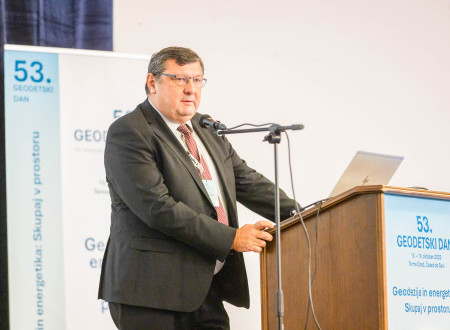 Govornik stoji za pultom s konferenčnim logotipom »53. geodetski dan« in nagovarja dvorano.