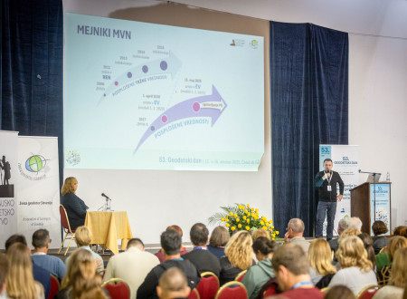 Predavatelj ob projekciji sheme z označenimi mejniki govori v polni dvorani.