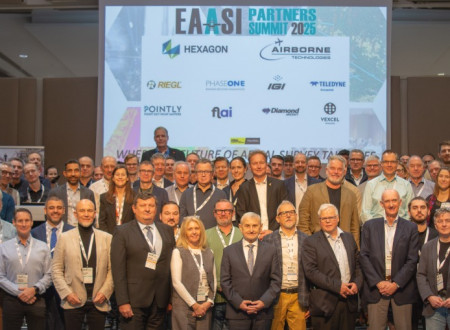 Velika skupina moških in žensk stoji pred projekcijskim platnom z logotipi partnerjev srečanja EAASI.