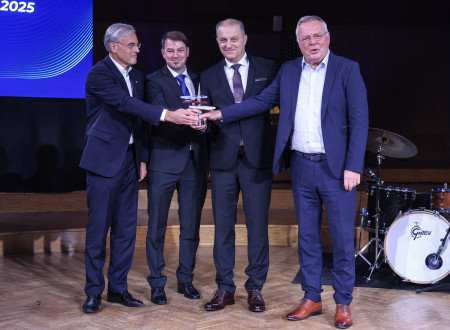 Štirje moški v poslovnih oblekah stojijo na odru in skupaj držijo stekleno-kovinsko nagrado.