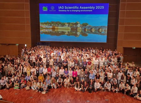 Velika skupina udeležencev stoji v dvorani pred velikim projekcijskim platnom.