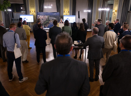 Ženska govori na govorniškem odru pred občinstvom v dvorani.