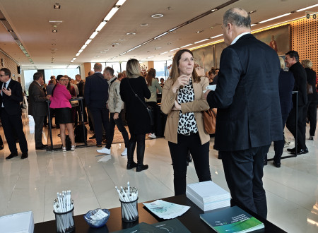 Predstavitvena miza Geodetske uprave z zloženkami Geo Slovenija in SLO4D, svinčniki in brošurami; v ozadju živahen pogovor udeležencev v preddverju Kongresnega centra Brdo.