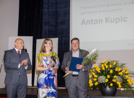 Moški s šopkom in listino stoji zraven podeljevalcev pred panoji ZGS.