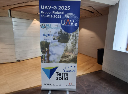 Samostoječ promocijski plakat z logotipi organizatorjev in napisom UAV-G 2025 stoji na hodniku konferenčnega centra.