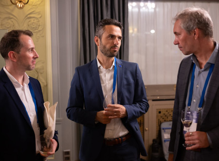 Trije moški v poslovnih oblekah se pogovarjajo in držijo kozarce.