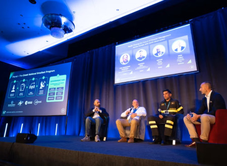 Več oseb sedi na odru v razpravi, ozadje prikazuje projekcijo panela.