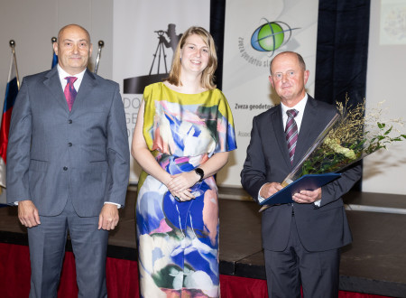 Moški s šopkom in priznanjem stoji na odru ob predstavnikih podeljevalca.