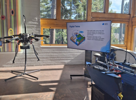 V sončno osvetljeni dvorani stoji velik letalski dron ob zaslonu z napisom Digital Twins.