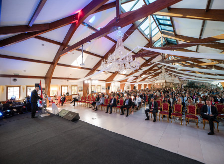 Velika konferenčna dvorana z lestenci in polnimi vrstami udeležencev, ki spremljajo program na odru.