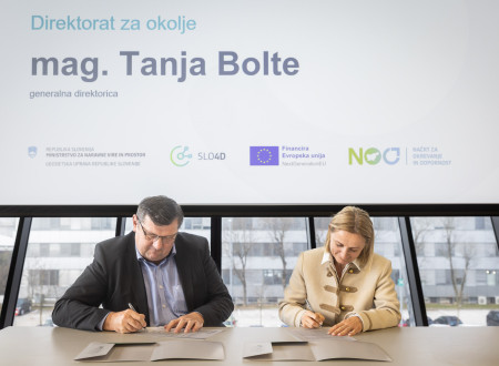 Moški in ženska sedita za mizo in kot predstavnika Direktorata za okolje ter Geodetske uprave RS podpisujeta dokumente, nad njima je projekcijsko platno z nazivom direktorata.