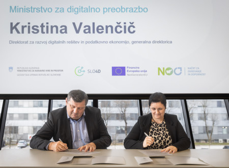 Moški in ženska sedita za mizo in kot predstavnika Ministrstva za digitalno preobrazbo ter Geodetske uprave podpisujeta dokumente o vzpostavitvi skupnosti Geo Slovenija.