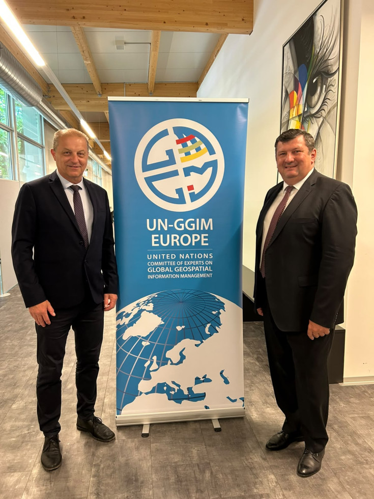 Dva moška v poslovnih oblekah stojita ob modrem panoju UN-GGIM: Europe.