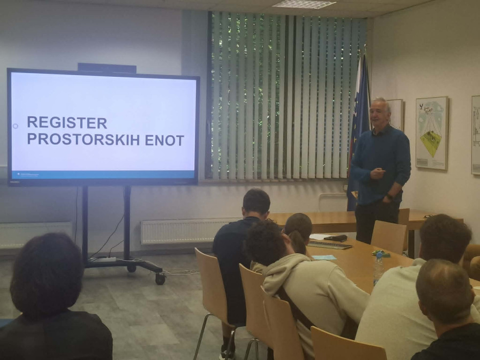 Moški stoji ob zaslonu s predstavitvijo Registra prostorskih enot, pred njim sedijo študenti v sejni sobi.