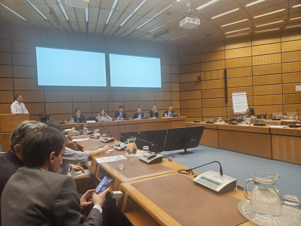 Udeleženci sedijo v konferenčni dvorani OZN na Dunaju med razpravo o integraciji geoprostorskih in statističnih informacij; na mizah so mikrofon, dokumenti in vrči z vodo.