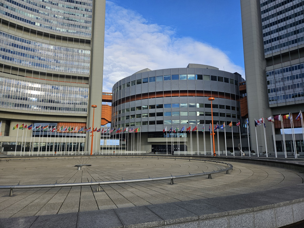 Sodobna zgradba sedeža Združenih narodov na Dunaju, pred katero stojijo zastave držav članic; objekt predstavlja prizorišče delavnice UN-GGIM.