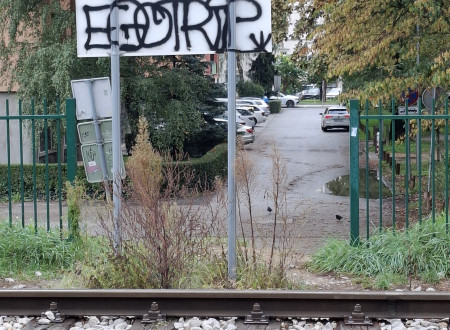 nezavarovan prehod čez želežniško progo, v ozadju pa je hrbtna stran prometnega znaka, ki je popisan s grafiti