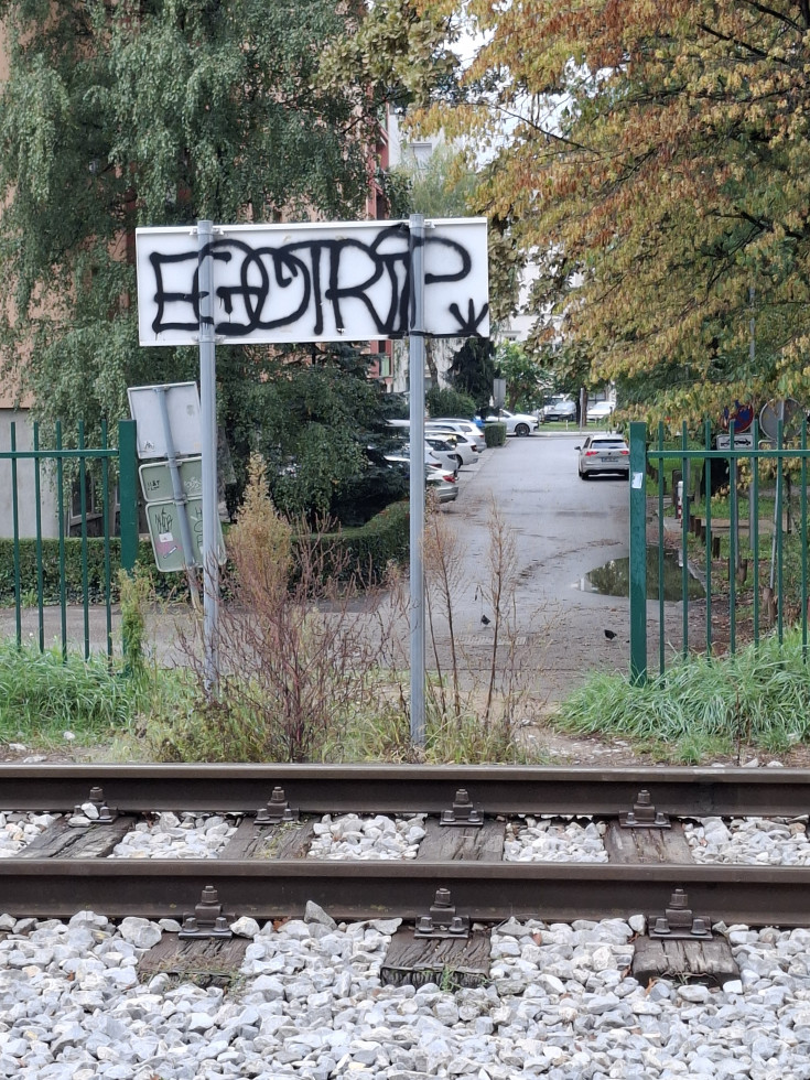 nezavarovan prehod čez želežniško progo, v ozadju pa je hrbtna stran prometnega znaka, ki je popisan s grafiti
