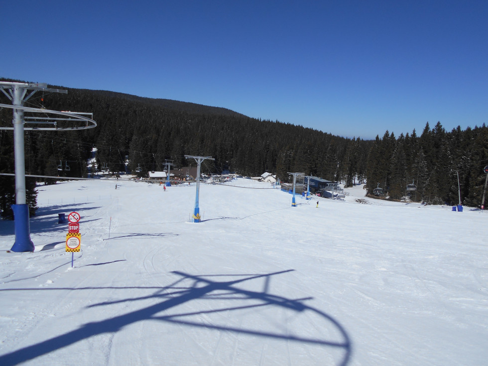 Smučišče na Rogli in žičniško napravo v delovanju. V ozadju je gozd in nebo je jasno in modro.