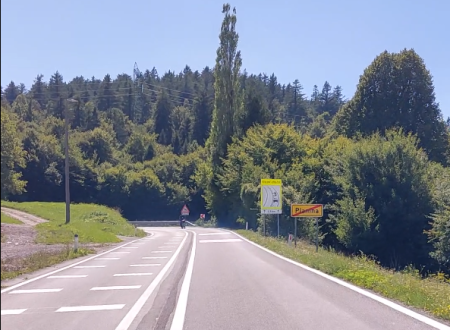 cesta z označeno talno označbo za motoriste. Na cesti je viden motorist, ki vozi v ovinek. Na desni strani ceste je vidna vertikalna signalizacija