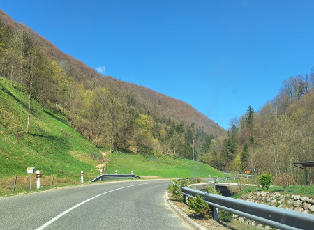 cesta, ki ima varnostno ograjo in prometno opremo za motoriste, v ozadju so hribi.